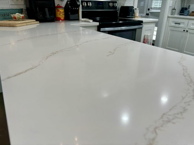 kitchen featuring light stone counters, stainless steel electric stove, and white cabinets