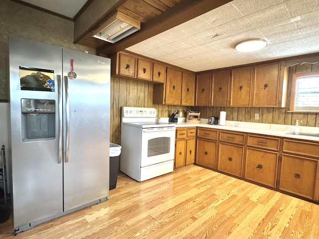 kitchen with brown cabinets, stainless steel refrigerator with ice dispenser, white electric range, light wood-style floors, and light countertops