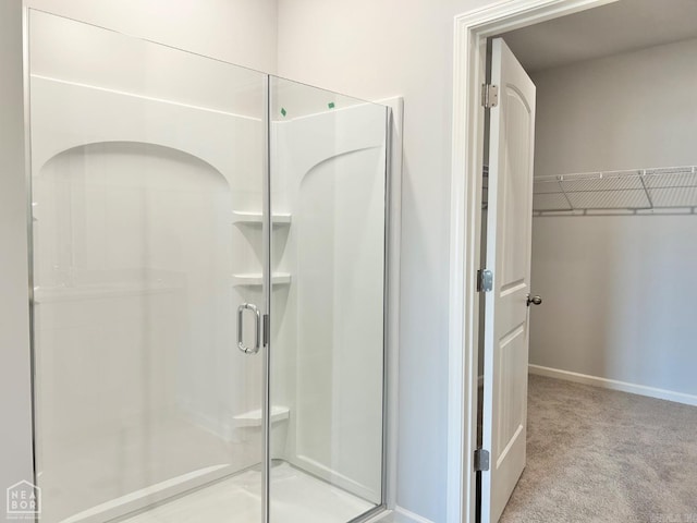 bathroom featuring a spacious closet, baseboards, and a stall shower