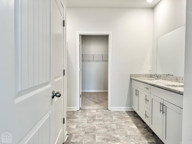 full bathroom featuring a walk in closet, double vanity, baseboards, and a sink