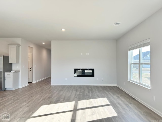 unfurnished living room featuring a glass covered fireplace, baseboards, visible vents, and light wood finished floors