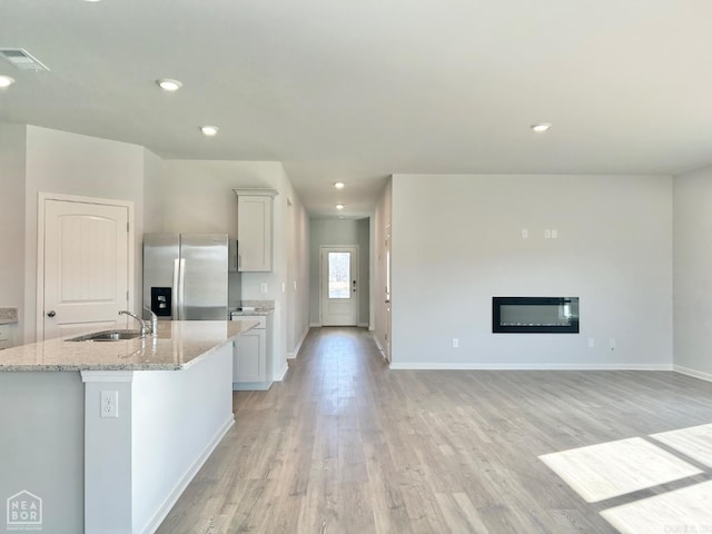 kitchen with visible vents, stainless steel refrigerator with ice dispenser, light stone counters, a glass covered fireplace, and light wood finished floors