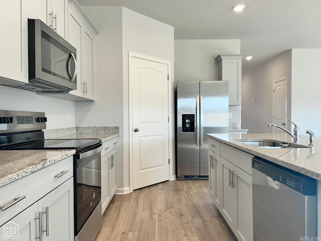 kitchen with light stone counters, light wood finished floors, a sink, stainless steel appliances, and white cabinetry