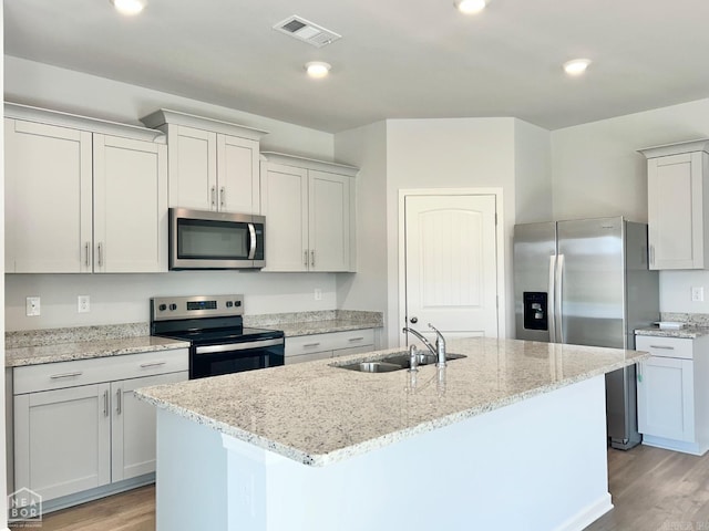 kitchen with light wood finished floors, visible vents, a sink, stainless steel appliances, and a kitchen island with sink