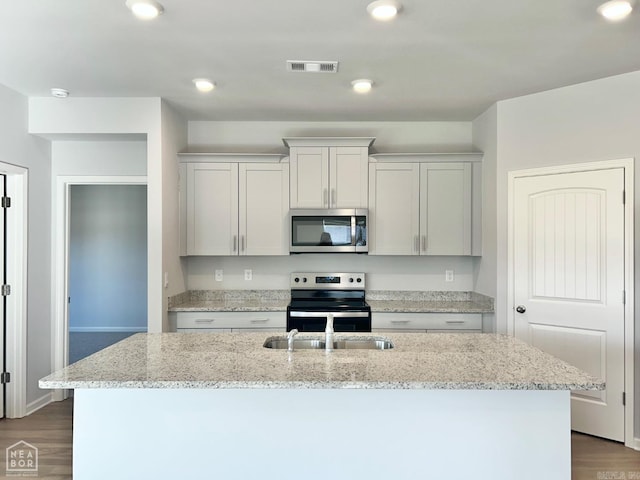 kitchen with visible vents, dark wood finished floors, light stone counters, appliances with stainless steel finishes, and a kitchen island with sink