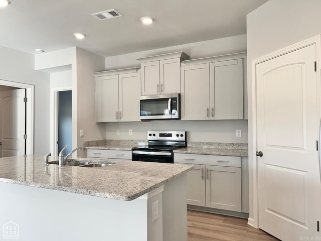 kitchen featuring visible vents, a sink, light stone counters, light wood-style floors, and appliances with stainless steel finishes