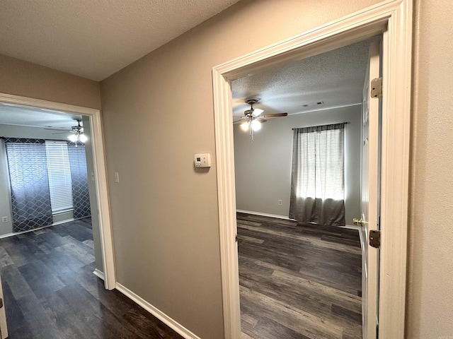 hall featuring dark wood-style floors, a textured ceiling, and baseboards