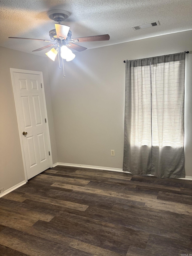 empty room with visible vents, a textured ceiling, dark wood finished floors, baseboards, and ceiling fan