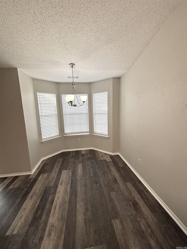 unfurnished dining area with visible vents, a notable chandelier, a textured ceiling, dark wood-style floors, and baseboards