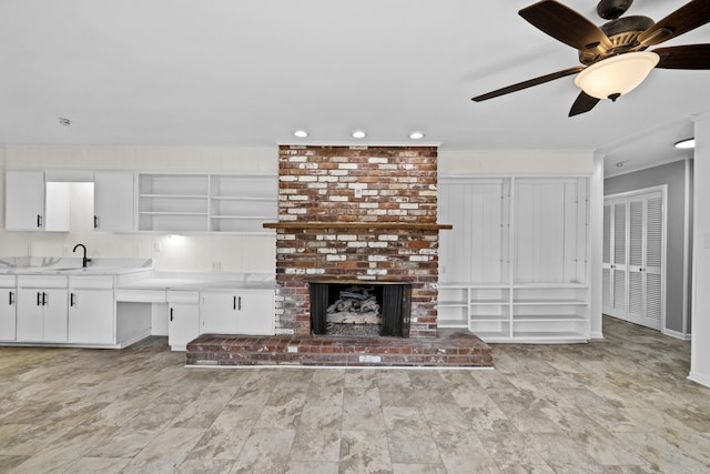 unfurnished living room with a brick fireplace, crown molding, ceiling fan, recessed lighting, and a sink