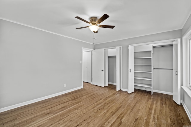 unfurnished bedroom with wood finished floors, crown molding, baseboards, and multiple closets