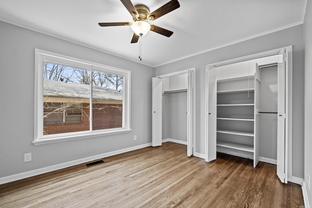 unfurnished bedroom with baseboards, wood finished floors, visible vents, and multiple closets