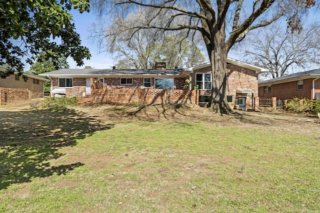 rear view of property with brick siding, a chimney, and a lawn