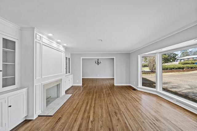 unfurnished living room with ornamental molding, wood finished floors, a fireplace, baseboards, and a chandelier