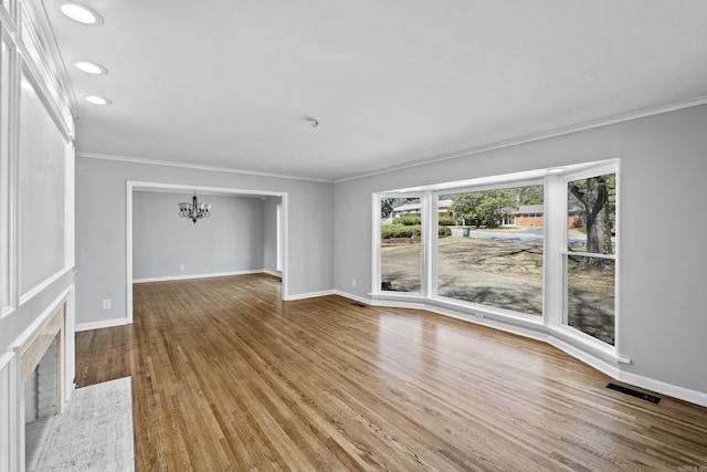 unfurnished living room featuring baseboards, wood finished floors, an inviting chandelier, and ornamental molding