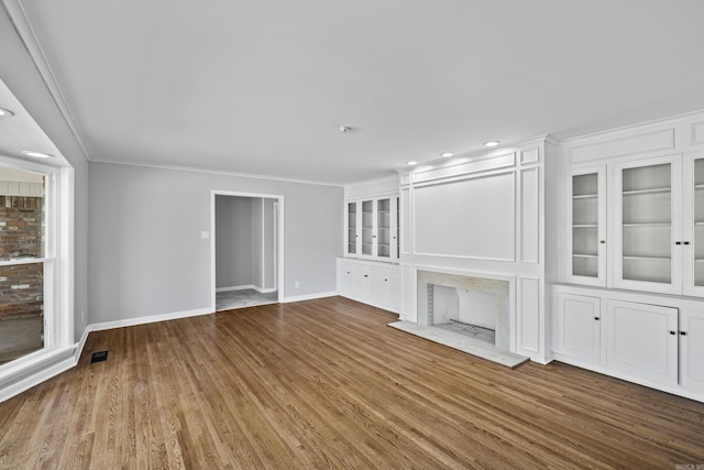 unfurnished living room featuring built in shelves, wood finished floors, baseboards, visible vents, and crown molding