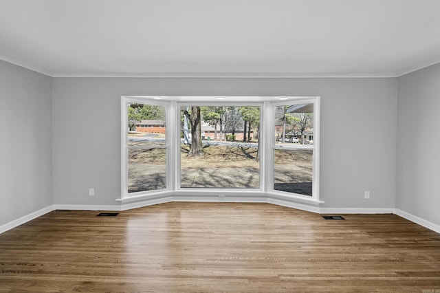 unfurnished room with a wealth of natural light, baseboards, wood finished floors, and ornamental molding