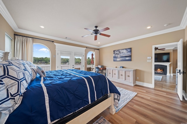 bedroom featuring light wood-style flooring, ornamental molding, access to outside, a glass covered fireplace, and french doors