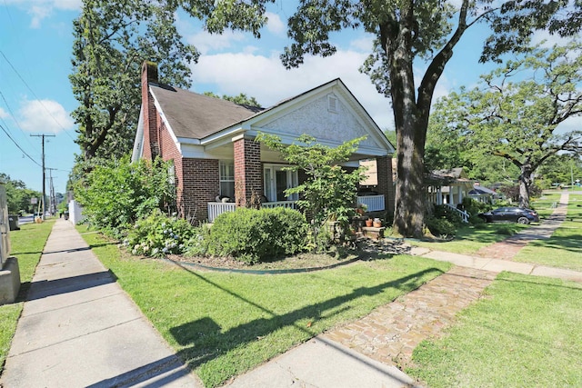 bungalow-style home with a front yard, a porch, brick siding, and a chimney