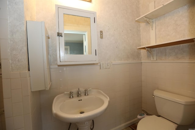 bathroom featuring a sink, toilet, tile walls, and wainscoting