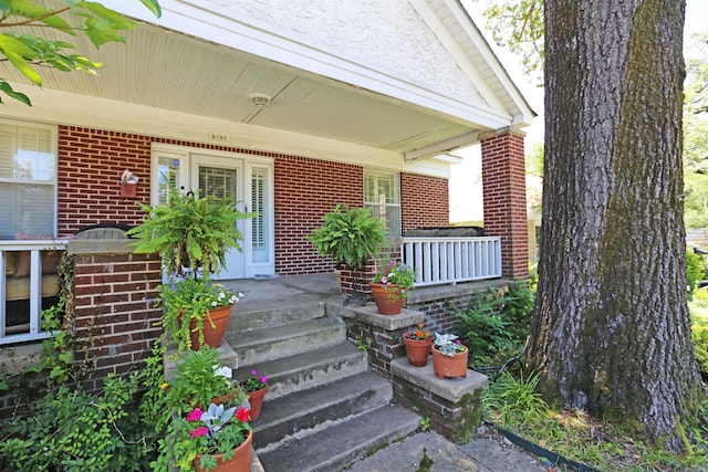 view of exterior entry featuring brick siding and covered porch