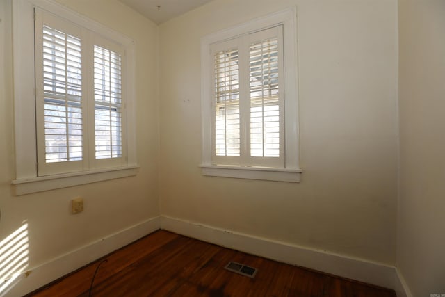 unfurnished room with dark wood finished floors, visible vents, plenty of natural light, and baseboards