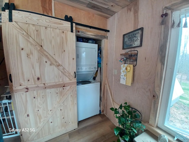 laundry area featuring stacked washer / drying machine, a barn door, wood finished floors, and laundry area