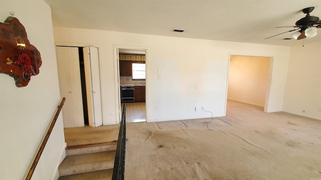 spare room with light carpet, visible vents, a textured ceiling, and a ceiling fan