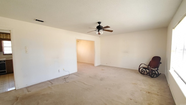 carpeted empty room with visible vents, a textured ceiling, and ceiling fan