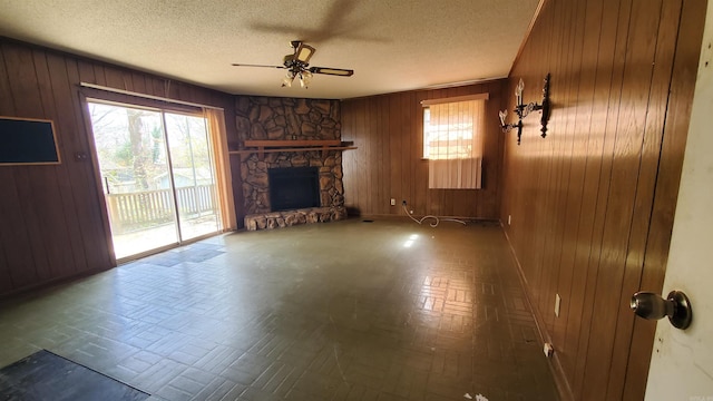 unfurnished living room featuring wooden walls, a ceiling fan, and a textured ceiling