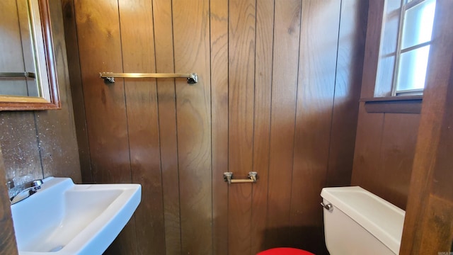 half bath with wooden walls, toilet, and a sink