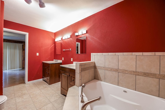bathroom featuring a ceiling fan, baseboards, two vanities, a whirlpool tub, and a sink