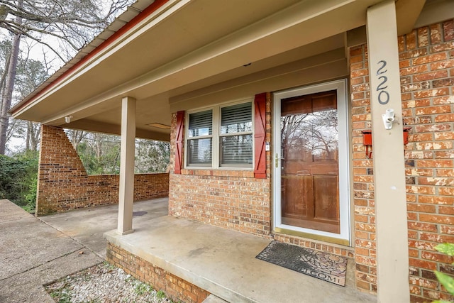 doorway to property featuring brick siding and a porch