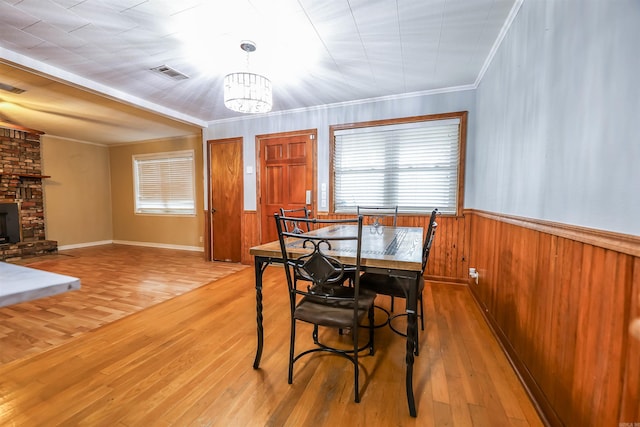dining space with light wood finished floors, a wainscoted wall, crown molding, and a notable chandelier