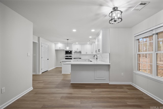 kitchen with visible vents, a peninsula, white cabinets, built in microwave, and dark wood-style flooring