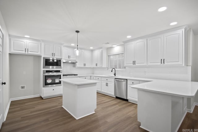 kitchen with under cabinet range hood, appliances with stainless steel finishes, a peninsula, white cabinets, and a sink