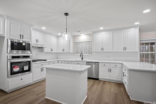 kitchen featuring under cabinet range hood, pendant lighting, appliances with stainless steel finishes, dark wood-style floors, and a sink