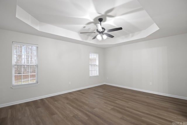 empty room featuring visible vents, baseboards, a tray ceiling, dark wood-style floors, and a ceiling fan