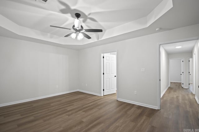 empty room featuring ceiling fan, baseboards, a raised ceiling, and dark wood-style floors