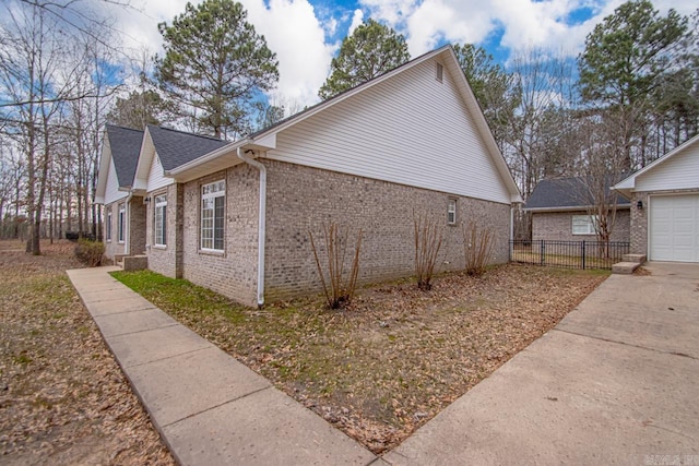 view of side of property with concrete driveway, fence, brick siding, and roof with shingles