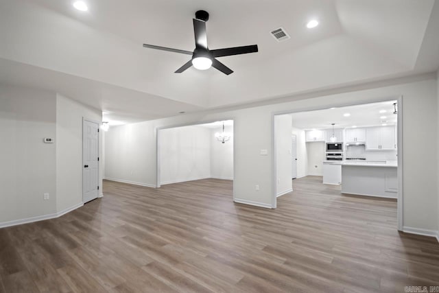 unfurnished living room featuring visible vents, a raised ceiling, ceiling fan, and wood finished floors