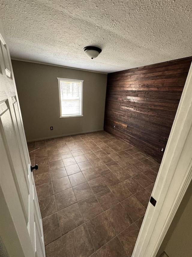 unfurnished room featuring dark tile patterned floors, wood walls, and a textured ceiling