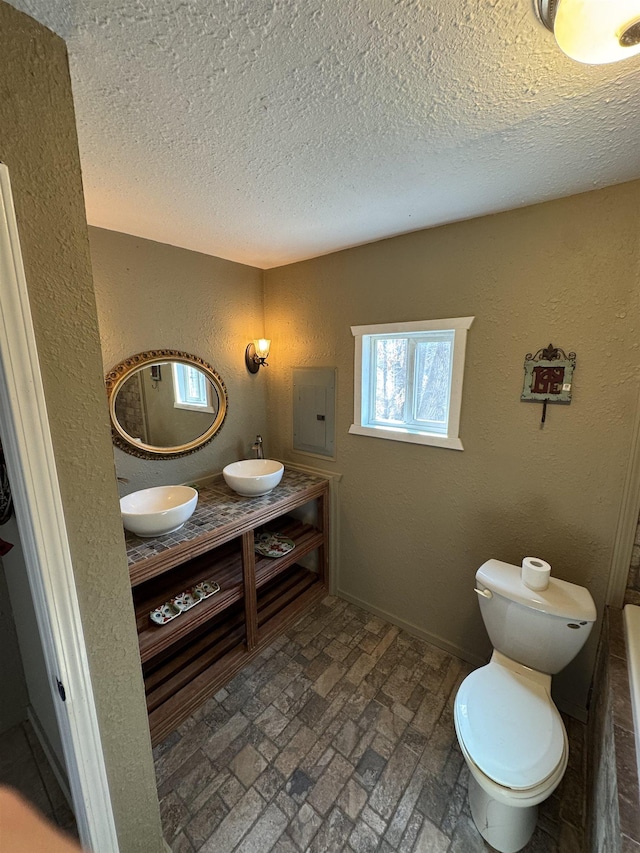 full bathroom with electric panel, a textured wall, brick floor, and a sink