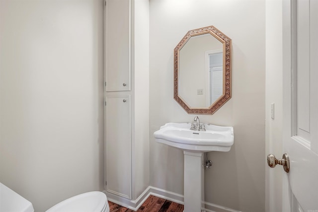 bathroom featuring toilet, wood finished floors, baseboards, and a sink