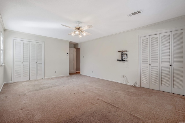 unfurnished bedroom featuring visible vents, multiple closets, baseboards, ornamental molding, and light carpet