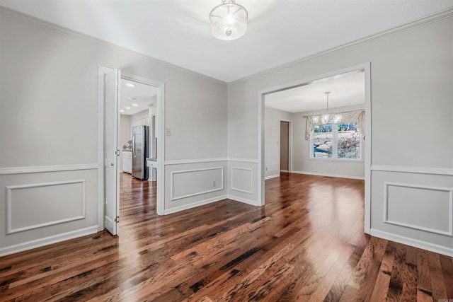 empty room with a wainscoted wall, an inviting chandelier, crown molding, a decorative wall, and dark wood-style flooring