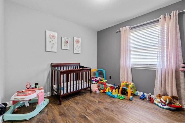 bedroom with a crib, baseboards, and wood finished floors