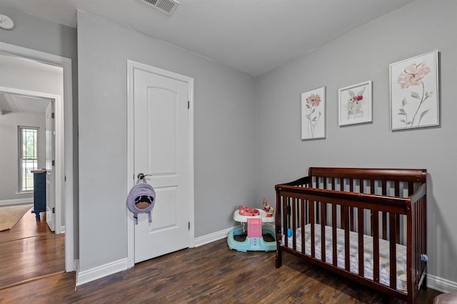 bedroom with a crib, visible vents, wood finished floors, and baseboards