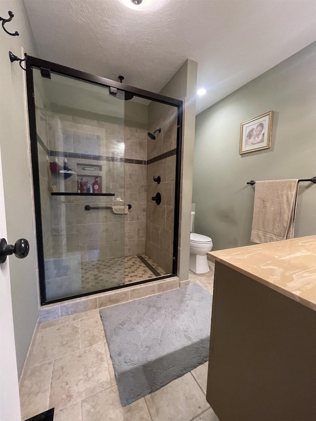 bathroom featuring toilet, a textured ceiling, a shower stall, baseboards, and vanity