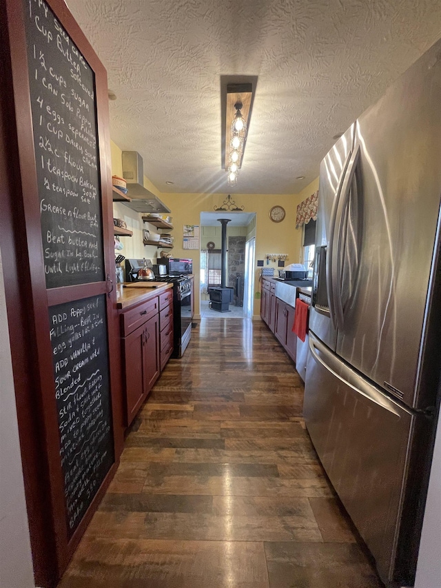 kitchen with gas stove, stainless steel fridge with ice dispenser, dark wood-type flooring, a textured ceiling, and wall chimney exhaust hood